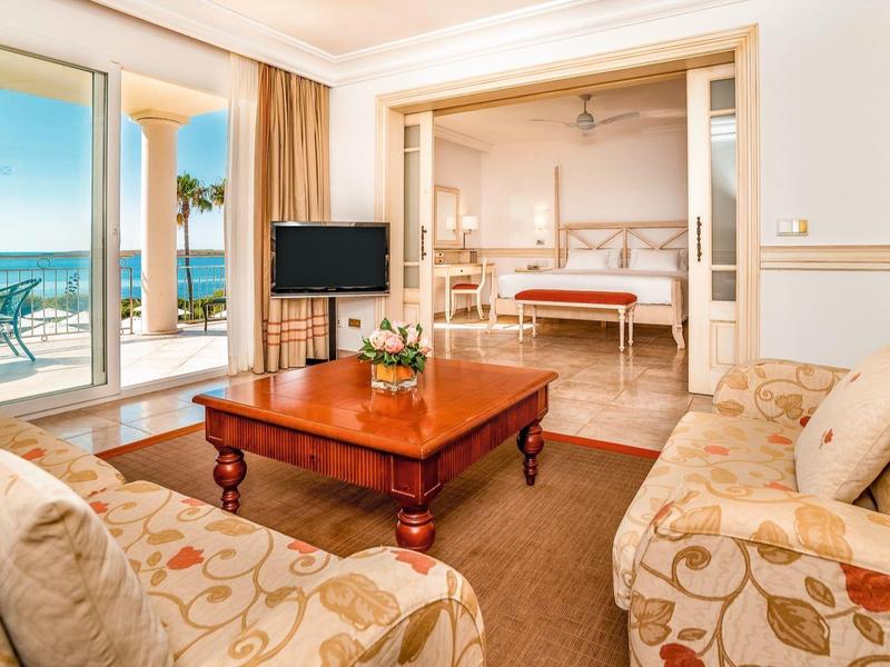 Bright hotel room with sea view, seating area, and adjoining bedroom.