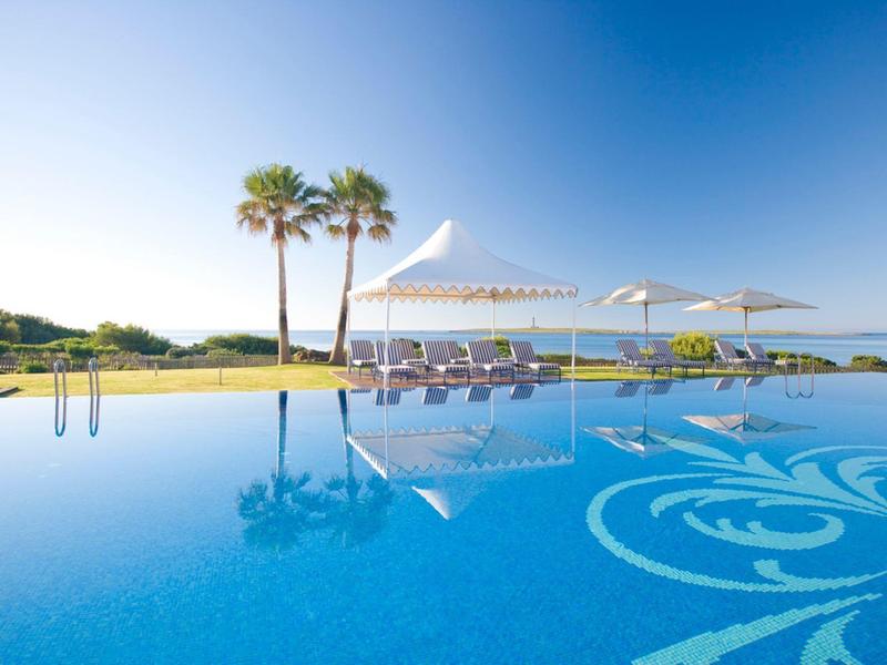 Large pool with sun umbrellas and palm trees in a sunny seaside setting