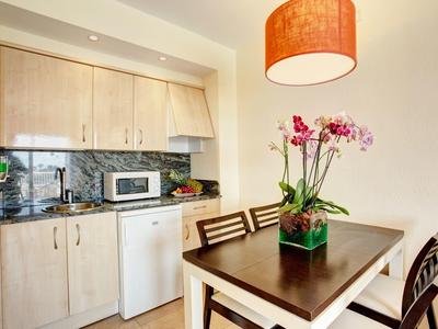 Compact kitchen with wooden cabinets, marble countertop, dining table with flowers, and pendant light.