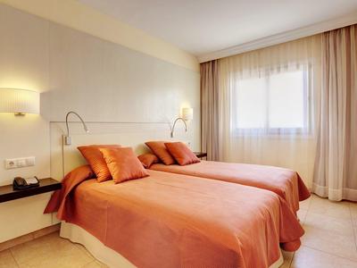 Cozy hotel room with two single beds, orange bedspreads, and warm lighting.