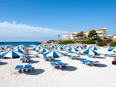 Beach with many blue lounge chairs and umbrellas under a clear sky.