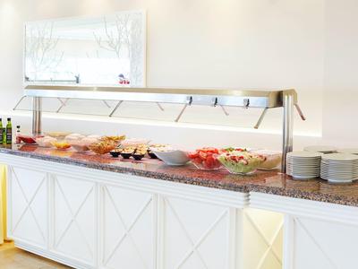 Buffet with cold dishes and plates in a bright room.
