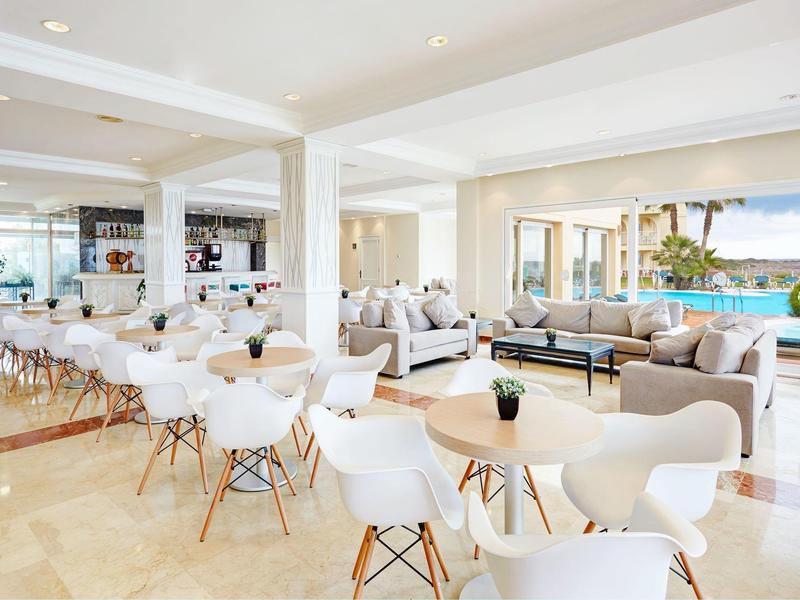 Bright, modern café with white chairs and large windows overlooking water.