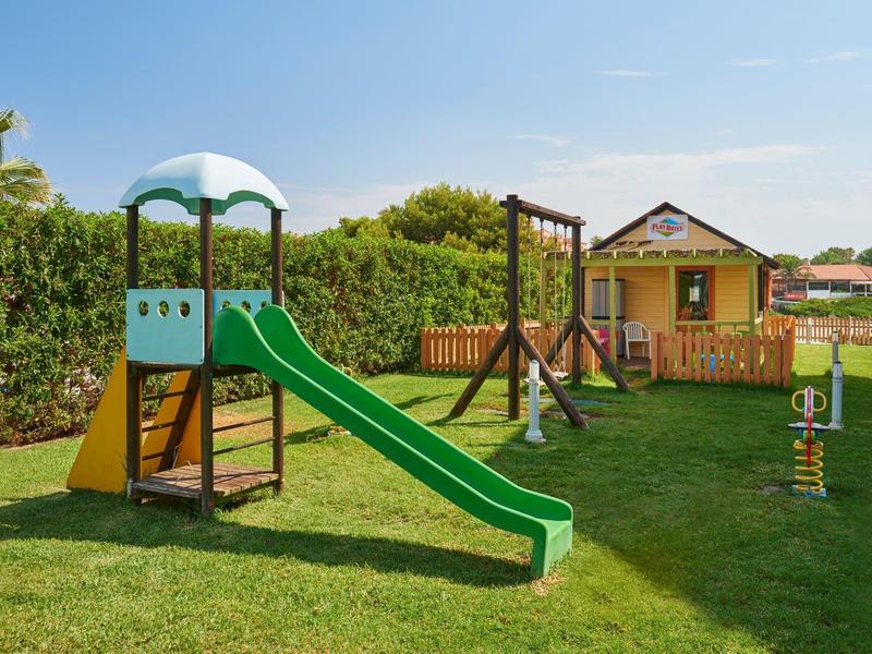 Children's playground with slide, swings, and climbing frame on grass near a house.