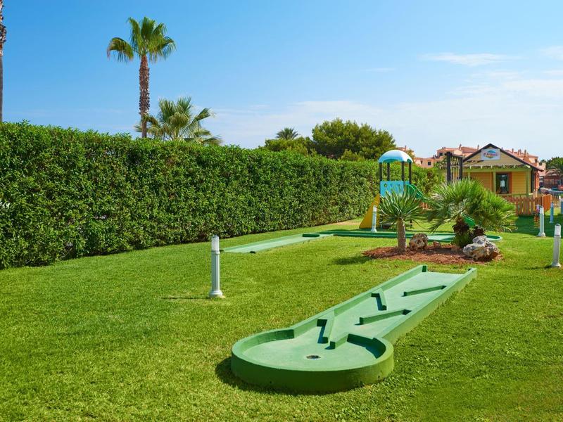 Mini golf course on well-maintained grass with palm trees and clear blue sky in the background.