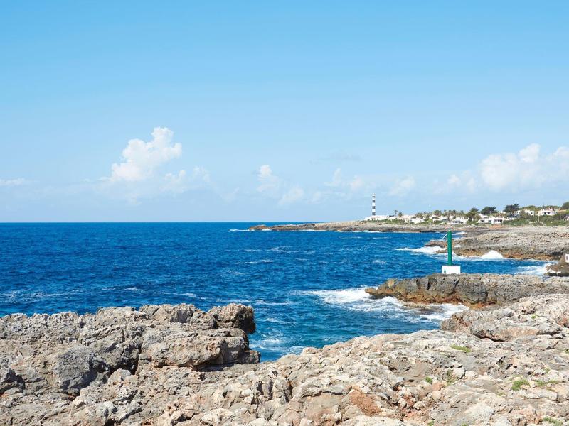 Rocky coast with blue sea and wide sky, buildings in the background.