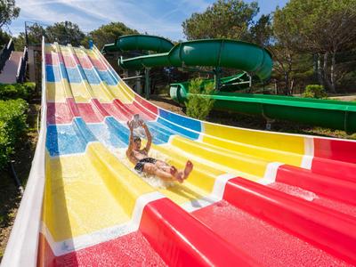 Person sliding down a wide, colorful water slide outdoors.