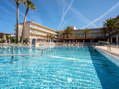 Hotel pool with clear blue water, surrounded by palm trees and hotel buildings under a blue sky.