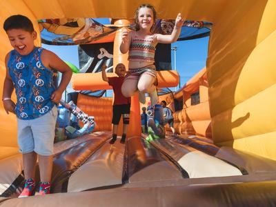 Children joyfully jumping on a large, yellow inflatable bouncy castle outdoors.