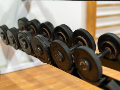 Row of black dumbbells on a rack in a fitness room with wooden flooring.
