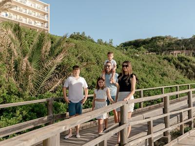 Five people walk on a wooden boardwalk with green vegetation under clear sky.