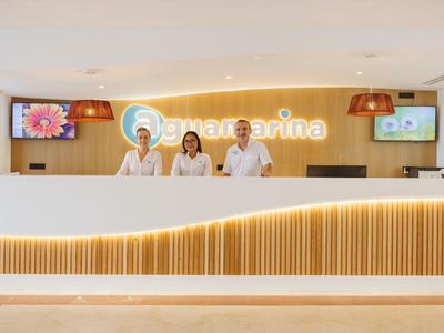 Hotel reception with three staff members behind a long, brightly lit desk.
