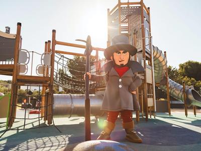 Child in gray coat stands on playground with climbing frame and slide in sunlight