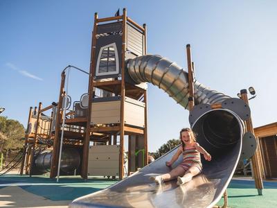 Child sliding down a large metal slide on a modern outdoor playground in daylight.