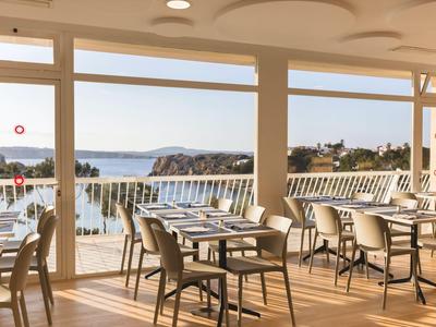 Elegant restaurant with wooden chairs and a view of the sea and coastline in daylight.