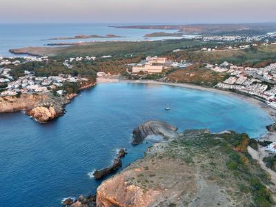 Coastal bay with clear blue water, surrounded by rocks and hotels along the beach.
