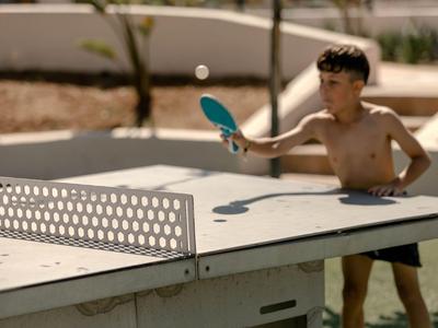 A boy is playing table tennis outside in sunny weather.