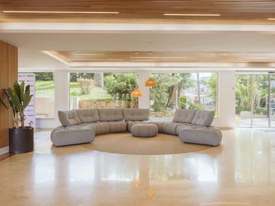 Bright hotel lounge with gray sofa set and large windows overlooking the garden.