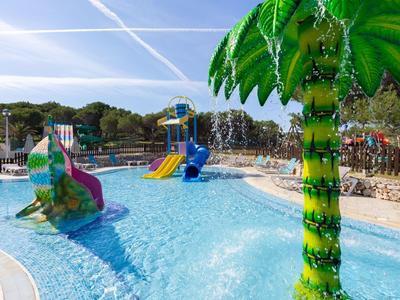 Children’s pool with water slides and a palm tree in a sunny hotel pool area.