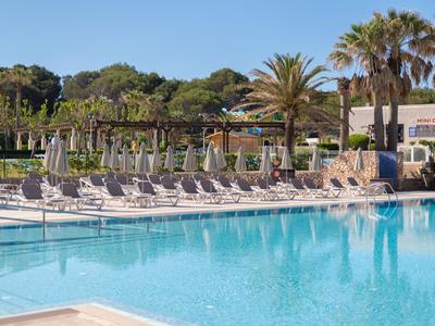 Large outdoor pool with lounge chairs, umbrellas, and palm trees in sunny weather.