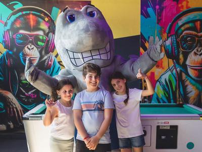 Three kids pose in front of a large plush figure in a colorful, artistic hotel lobby.