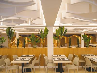 Modern restaurant with set tables, upholstered chairs, and plants as decoration.