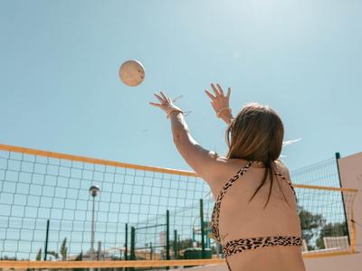 Woman in swimsuit playing beach volleyball under sunny clear sky.