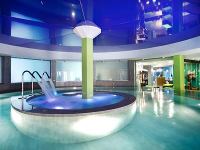 Moderner Innenpool mit rundem Whirlpool und Wasserspielen unter blauem Licht.