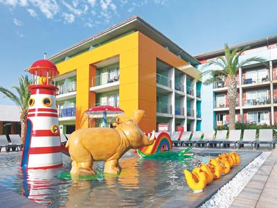 Kolorowy basen na zewnątrz z figurą żyrafy, latarnią morską i budynkiem hotelu w tle