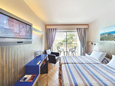 Helles Hotelzimmer mit Doppelbett, Flachbildfernseher und Balkon mit Blick ins Grüne.