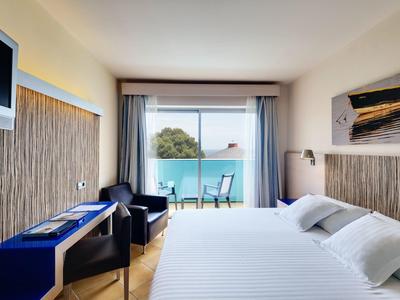 Nowoczesny pokój hotelowy z podwójnym łóżkiem, telewizorem, biurkiem i balkonem z widokiem na morze.