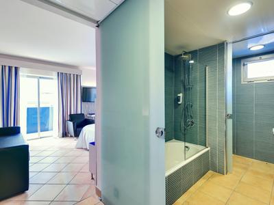 Nowoczesny pokój hotelowy z widokiem na jasną sypialnię obok łazienki z wanną i prysznicem.