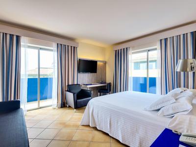 Nowoczesny pokój hotelowy z dużym łóżkiem, zasłonami z niebieskimi akcentami i balkonem.