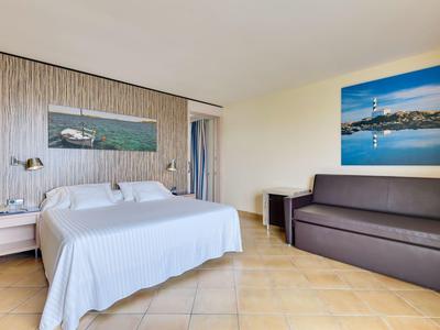 Jasny pokój hotelowy z podwójnym łóżkiem, stolikami nocnymi, obrazami na ścianie i brązową sofą