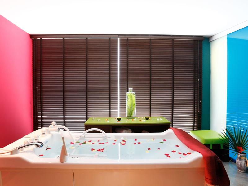 Jacuzzi z czerwonymi i niebieskimi ścianami, zielonymi krzesłami i zamkniętymi żaluzjami w tle.