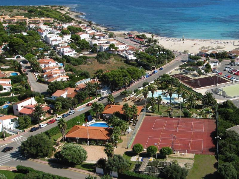 Widok z lotu ptaka na nadmorską wioskę z plażą, kortami tenisowymi i terenami zielonymi.