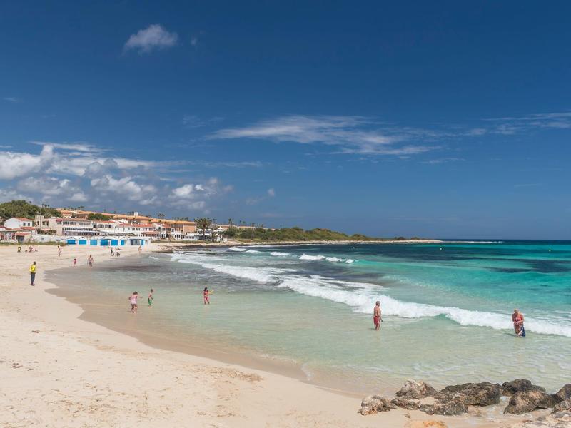 Plaża z białym piaskiem, czystą turkusową wodą i budynkami w tle w słoneczny dzień.