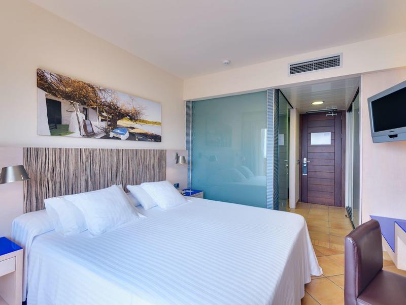 Nowoczesny pokój hotelowy z dwoma pojedynczymi łóżkami, szklaną ścianką łazienkową i telewizorem ściennym.