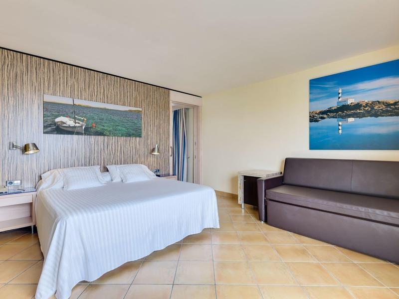 Jasny pokój hotelowy z podwójnym łóżkiem, stolikami nocnymi, obrazami na ścianie i brązową sofą