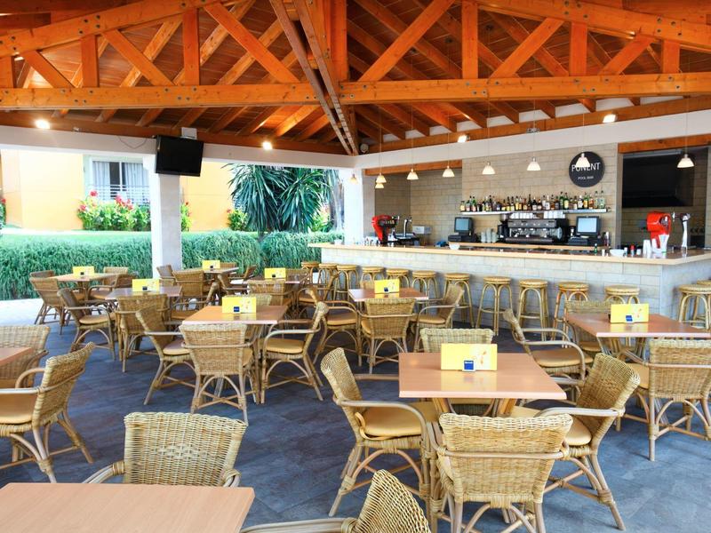 Zadaszony taras na zewnątrz z drewnianymi krzesłami i stołami przed barem hotelowym