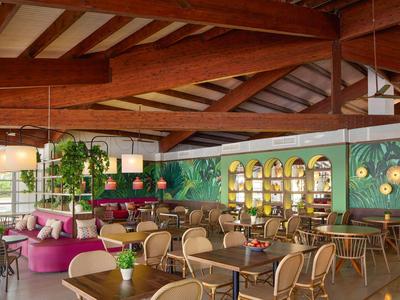 Příjemná restaurace s dřevěnými trámy na stropě, barevným posezením a zelenými nástěnnými dekoracemi.