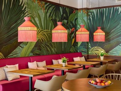 Pohodlný hotelový lounge s červenými pohovkami, dřevěnými stoly a tropickou výzdobou stěn.