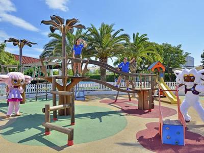 Barevné dětské hřiště s lezeckými konstrukcemi a postavami pod modrou oblohou.