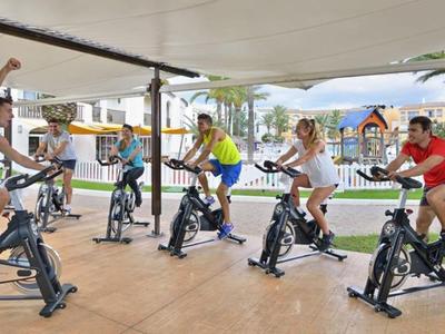 Gruppe von sechs Personen trainiert gemeinsam auf Spinning-Bikes unter einem Pavillon im Freien.