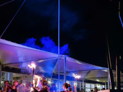 Zwei Feuerspucker führen vor Publikum unter einem überdachten Bereich bei Nacht auf.