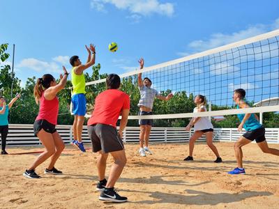 Gruppe von Menschen spielt Beachvolleyball auf Sandplatz bei sonnigem Wetter.