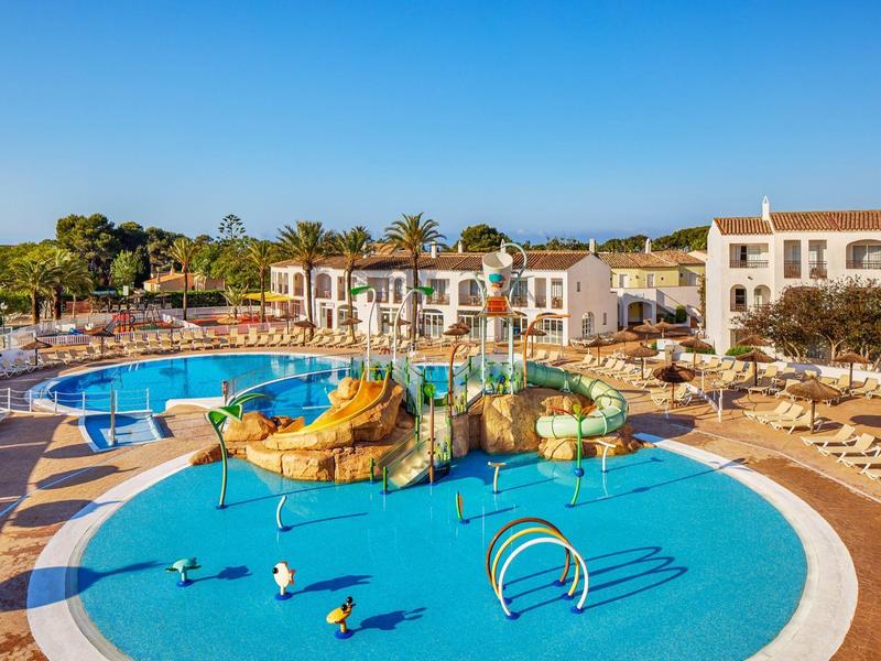 Velký bazén s vodním hřištěm v slunečném hotelovém resortu s mnoha lehátky.