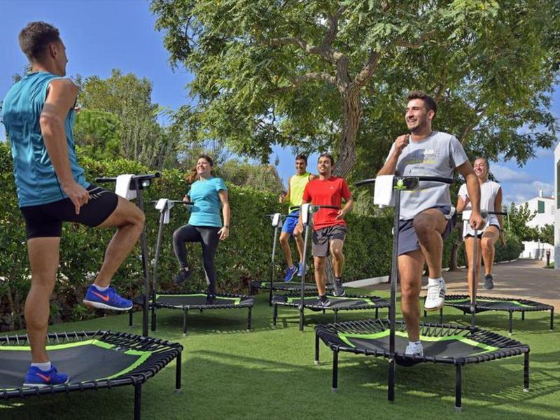 Skupina provádějící fitness cvičení na trampolínách venku pod stromy