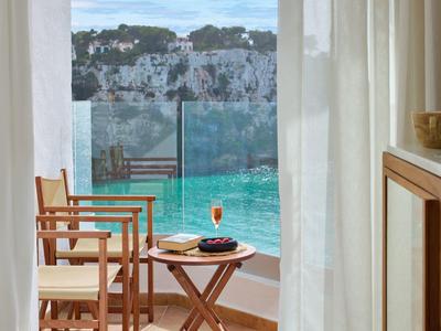 Balkon met twee houten stoelen en klein tafeltje met drankje, uitzicht op water en witte kliffen.