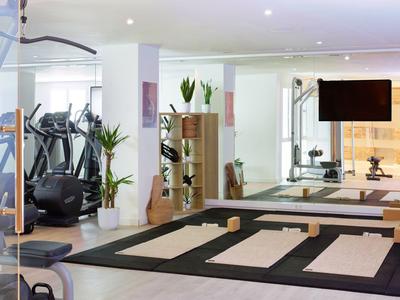 Moderner Fitnessraum mit Laufbändern, Spiegelwand und Trainingsmatten in einem Hotel.